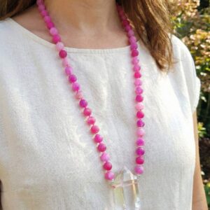 Woman wearing long pink gemstone mala necklace with quartz crystal pendant, styled with a white linen top for a bohemian look.