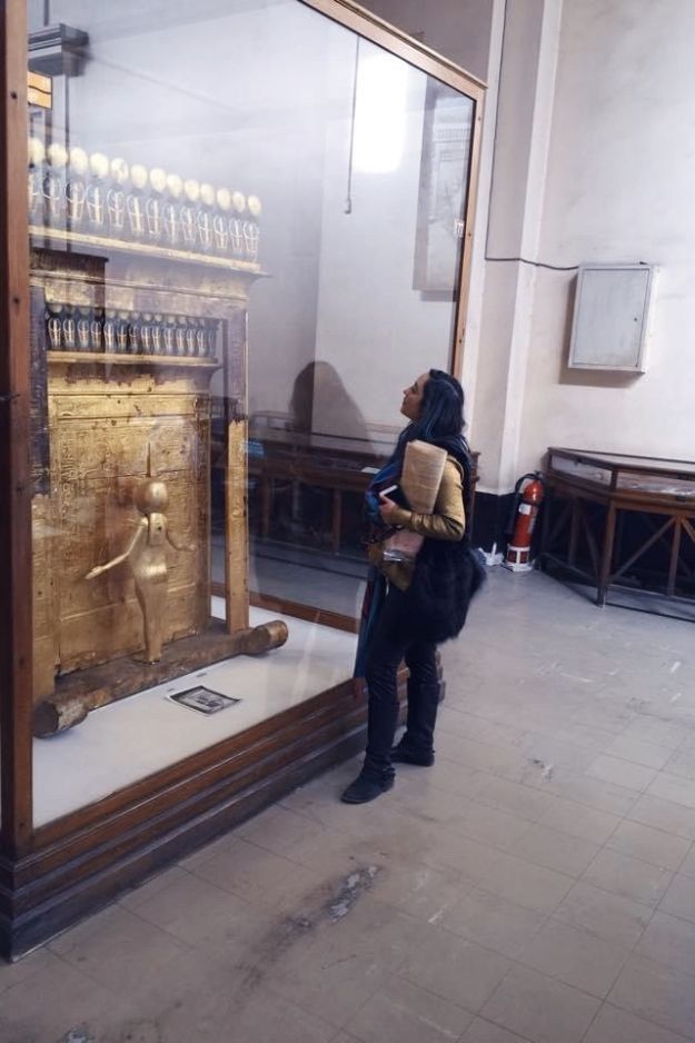 A woman admiring a golden ancient Egyptian artifact on display at the Cairo Museum, reflecting on Egypt's rich history and craftsmanship.