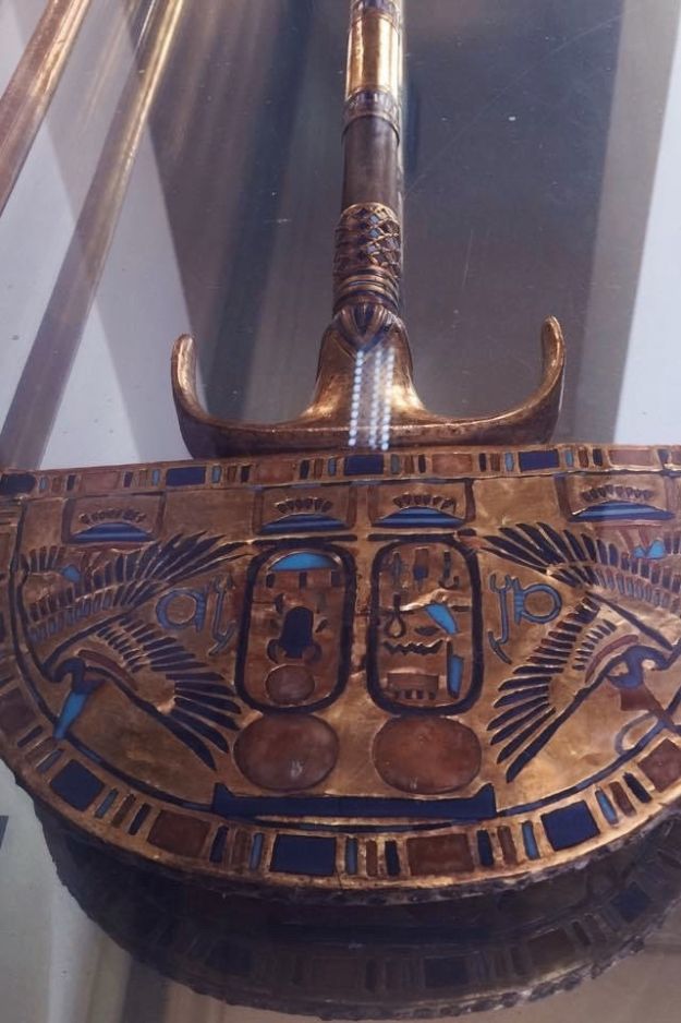A detailed close-up of an ancient Egyptian gold scepter, showcasing intricate designs and symbols, displayed in a museum exhibit.
