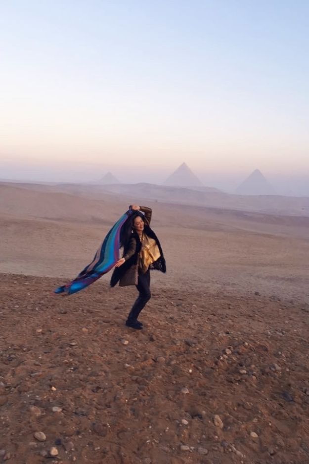 A woman joyfully dancing in the desert with the Pyramids of Giza in the background, capturing a carefree moment in Egypt.