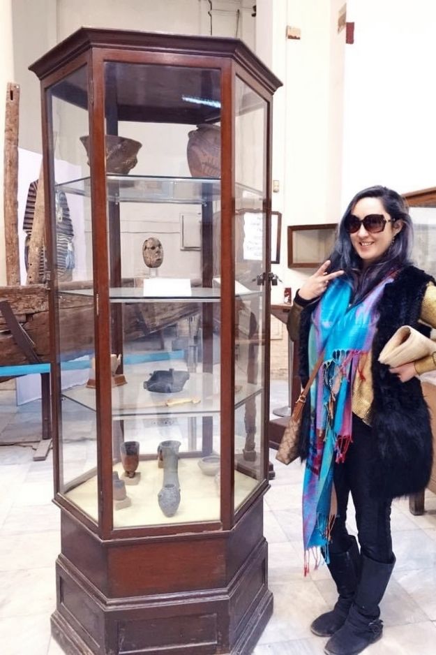 A woman posing next to a display case of ancient Egyptian artifacts at the Cairo Museum, showcasing the exploration of Egypt's rich history.