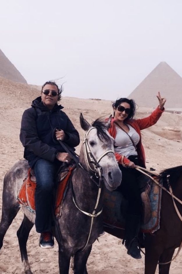 A couple riding horses in front of the Pyramids of Giza, Egypt, enjoying an adventure in the desert landscape.