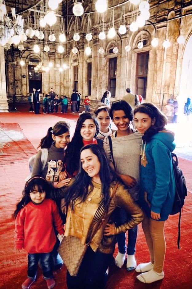 A woman posing with a group of children inside the beautifully lit interior of the Mohammed Ali Mosque in Cairo, Egypt.