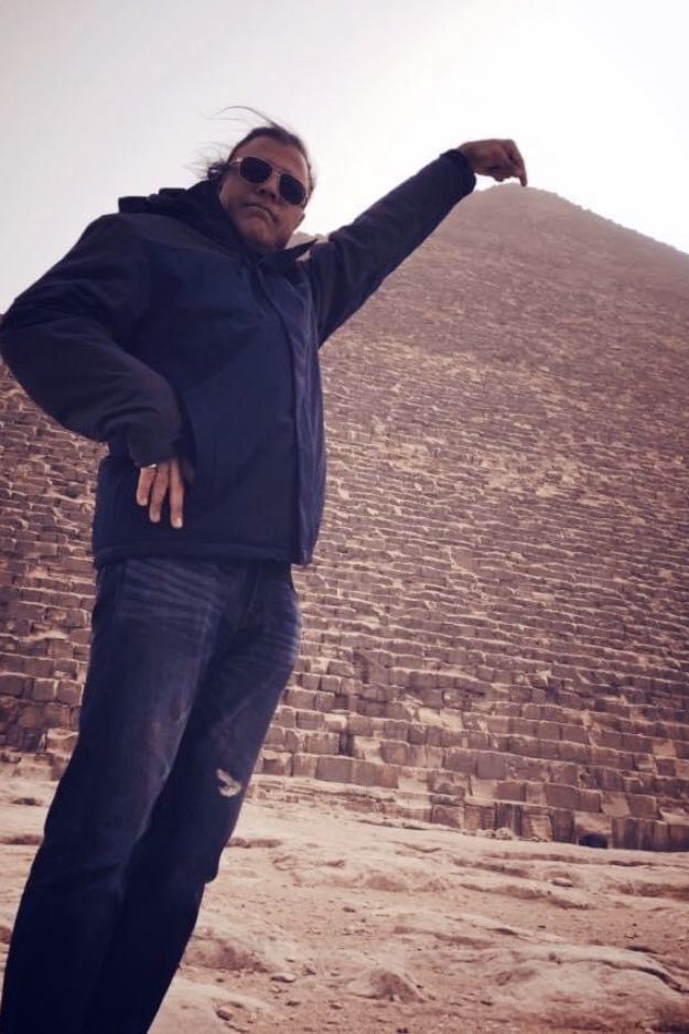 A man posing as if he's holding the tip of the Great Pyramid of Giza, creating a fun and playful illusion in front of the ancient wonder in Egypt.