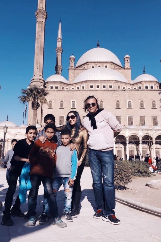 A couple posing with local children in front of the Mohammed Ali Mosque in Cairo, Egypt, capturing a spontaneous and joyful moment during their visit.
