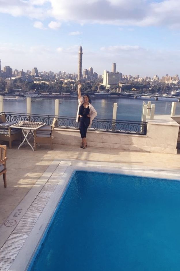 A woman standing on a rooftop with a view of the Nile River and Cairo Tower in the background, enjoying the cityscape of Cairo, Egypt.