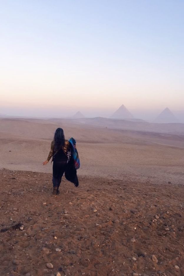 A woman walking towards the Pyramids of Giza across the desert, capturing a serene and contemplative moment in Egypt.