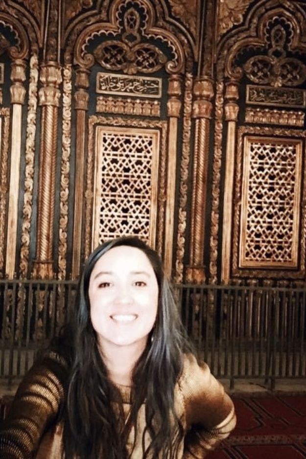 A woman smiling inside a historic mosque in Cairo, Egypt, with ornate architectural details in the background.