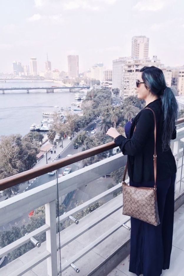A woman overlooking the Nile River and the Cairo skyline from a balcony, capturing a moment of reflection in Egypt's bustling capital.