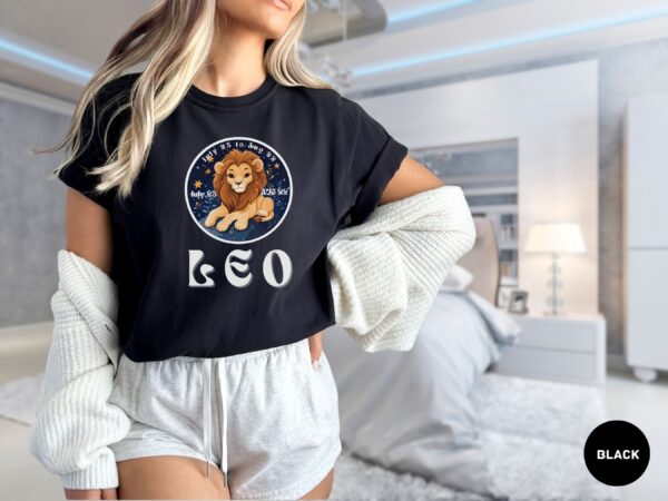 Woman wearing a black Comfort Colors 1717 t-shirt with a Leo Zodiac design featuring a cute lion illustration, stars, and the dates "July 23 to Aug 22."