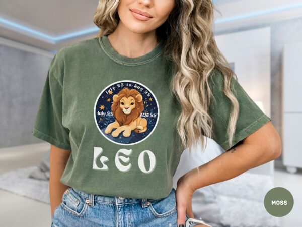 Woman wearing a Moss Comfort Colors 1717 t-shirt with a Leo Zodiac design featuring a cute lion illustration, stars, and the dates "July 23 to Aug 22."