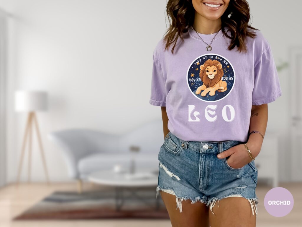 Woman wearing an Orchid Comfort Colors 1717 t-shirt with a Leo Zodiac design featuring a cute lion illustration, stars, and the dates "July 23 to Aug 22."