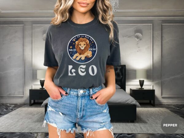 Woman wearing a Pepper Comfort Colors 1717 t-shirt with a Leo Zodiac design featuring a cute lion illustration, stars, and the dates "July 23 to Aug 22."