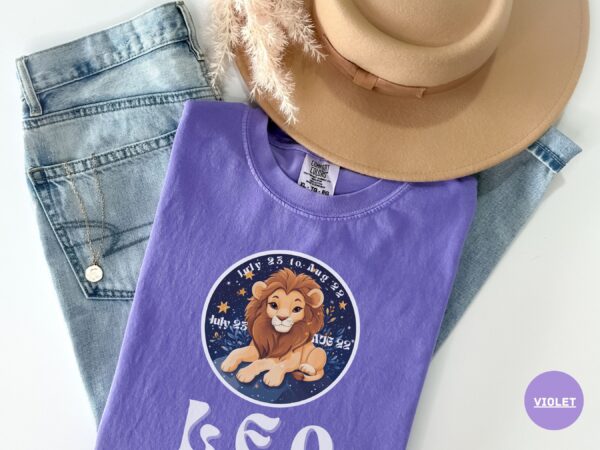 Flat lay of a Violet Comfort Colors 1717 t-shirt with a Leo Zodiac design featuring a cute lion illustration, stars, and the dates "July 23 to Aug 22."