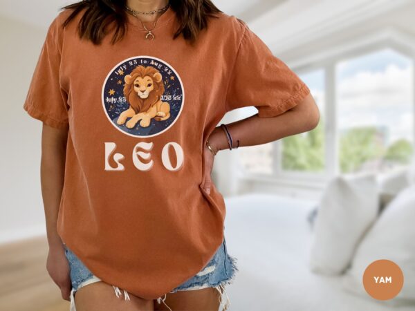 Woman wearing a Yam Comfort Colors 1717 t-shirt with a Leo Zodiac design featuring a cute lion illustration, stars, and the dates "July 23 to Aug 22."