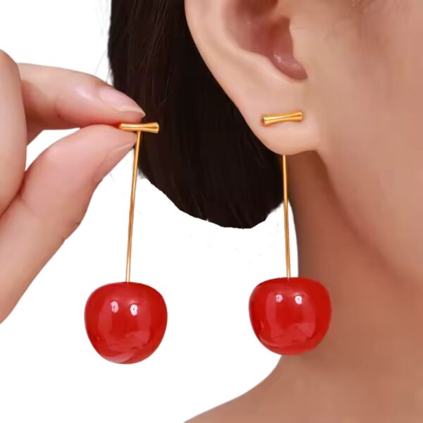Model wearing cherry drop earrings with gold stems and red resin cherries