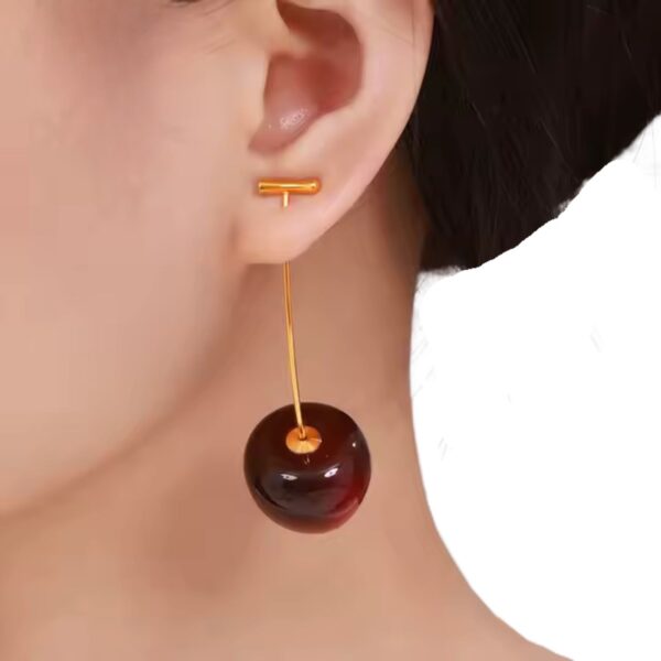 Model wearing dark cherry drop earrings with gold-plated stem