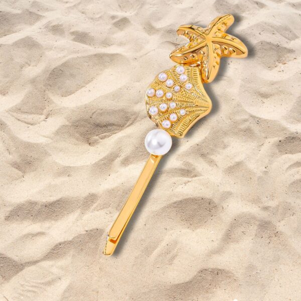 Gold seashell and starfish hair clip with pearl detail resting on beach sand