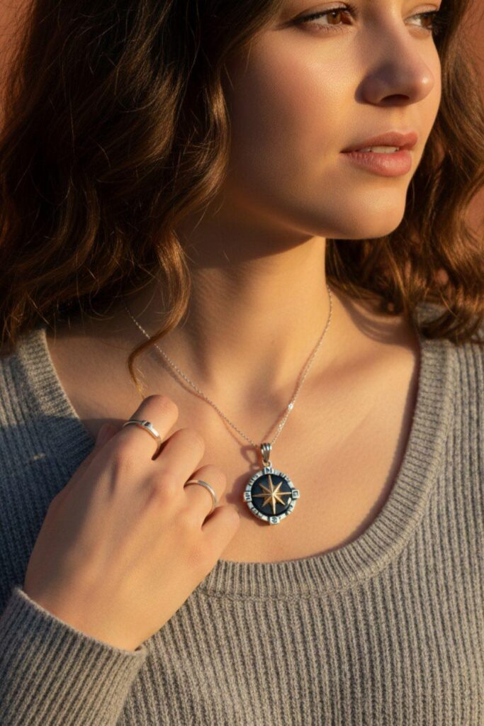 Close-up of a model wearing a silver north star compass necklace with a central gold star over a grey textured sweater