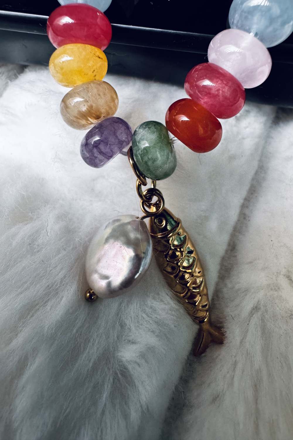 macro close up of colorful gemstone beads pearl charm and gold fish pendant necklace detail