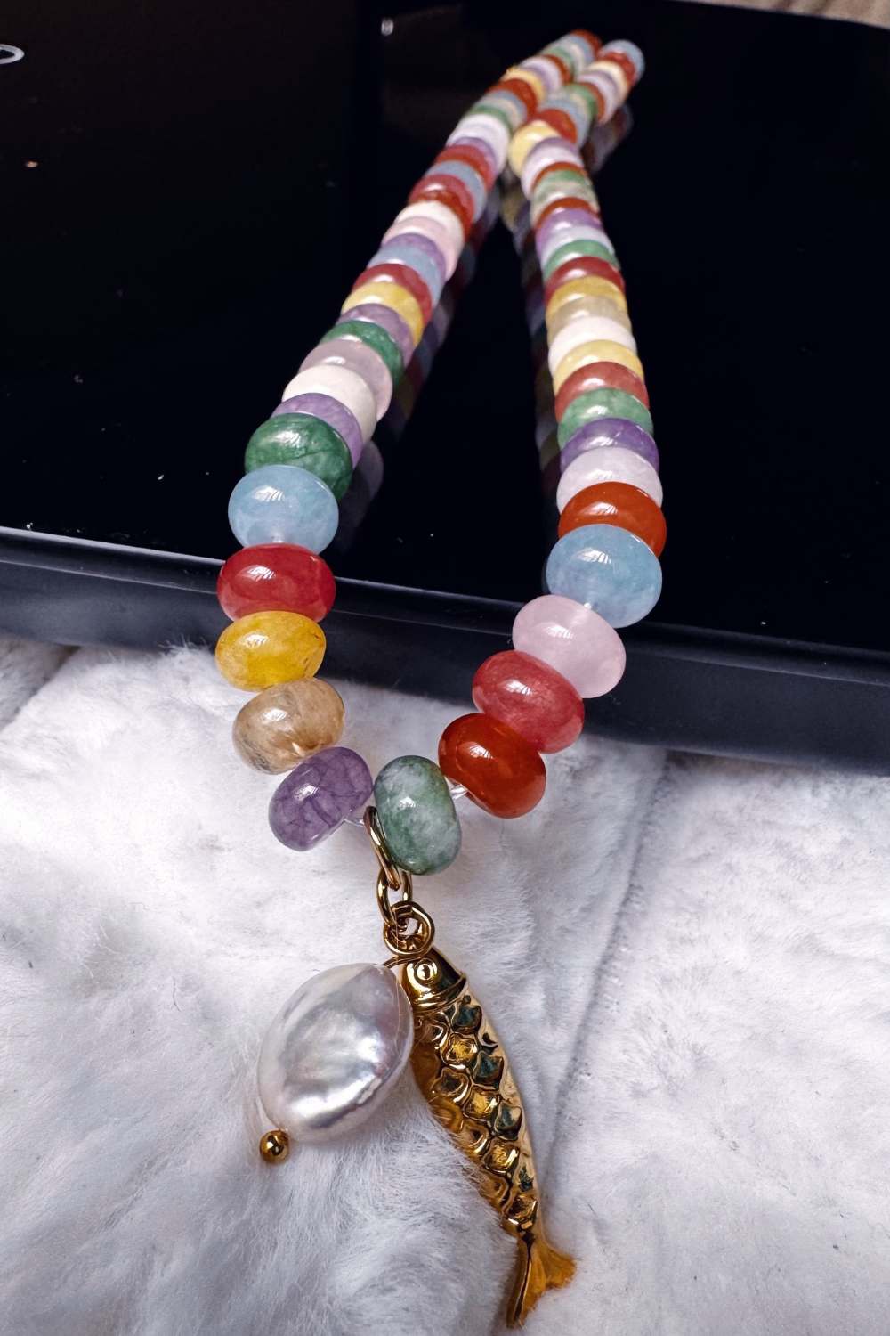 natural gemstone beaded necklace with gold fish pendant and pearl charm close up reflection detail